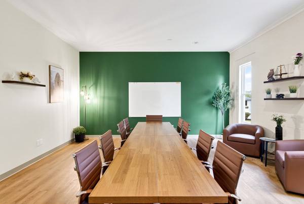 Long conference table lined with leather chairs facing a whiteboard, plant shelves along the side wall