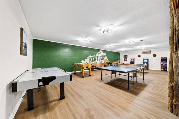 Air hockey and ping pong tables in a game room with a green Kentucky mural and arcade machines