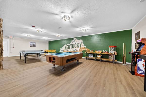 Wide game room with ping-pong and pool tables, a popcorn cart and snack shelves along a green wall