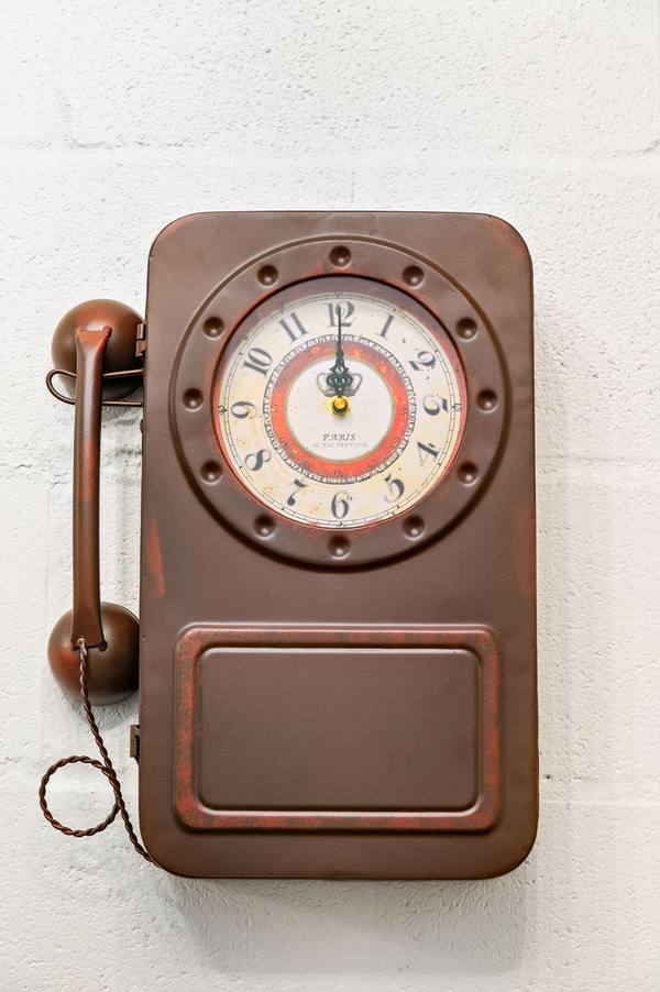 Antique-style brown wall telephone with a clock face mounted on a white painted brick wall