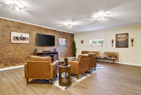 Leather armchairs and a loveseat facing a wall-mounted TV, with a wooden bench along a cream block wall