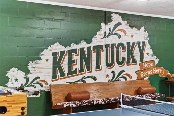 Hand-painted Kentucky mural reading Hope Grows Here above a cowhide bench and foosball table