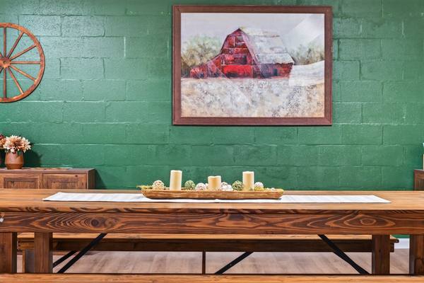 Wooden table with a candle centerpiece below a framed red barn painting on a green block wall
