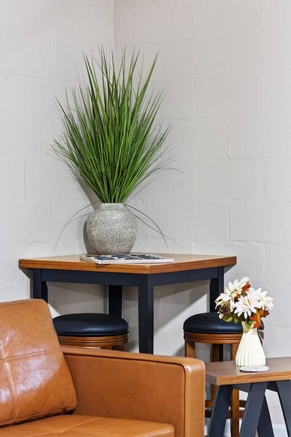Corner table with a checkers board, two stools and a tan leather armchair against a white brick wall