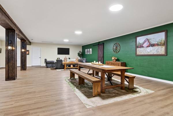 Open common room with a farmhouse table and benches, green block wall, and a TV lounge beyond