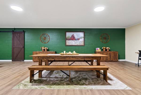 Wooden farmhouse table with benches on a rug, sliding barn door and a barn painting on a green wall