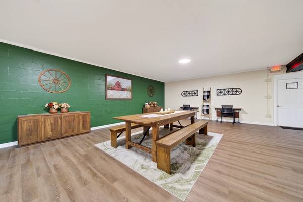Open room with a long farmhouse table and benches, green accent wall, wagon wheel and barn painting