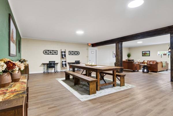 Long farmhouse table with benches and tan leather sofas in the lounge beyond a timber beam