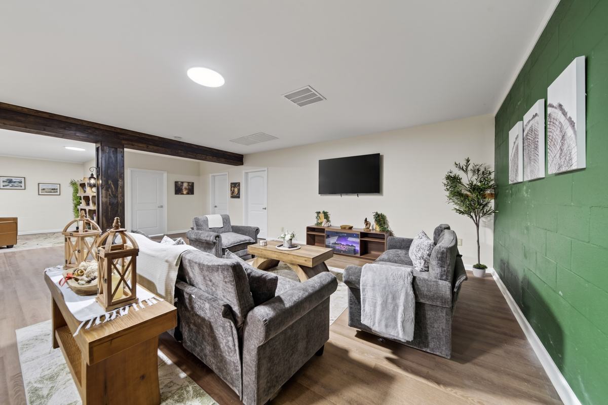 Upholstered armchairs with throws around a coffee table beside a lit fireplace under a wood beam