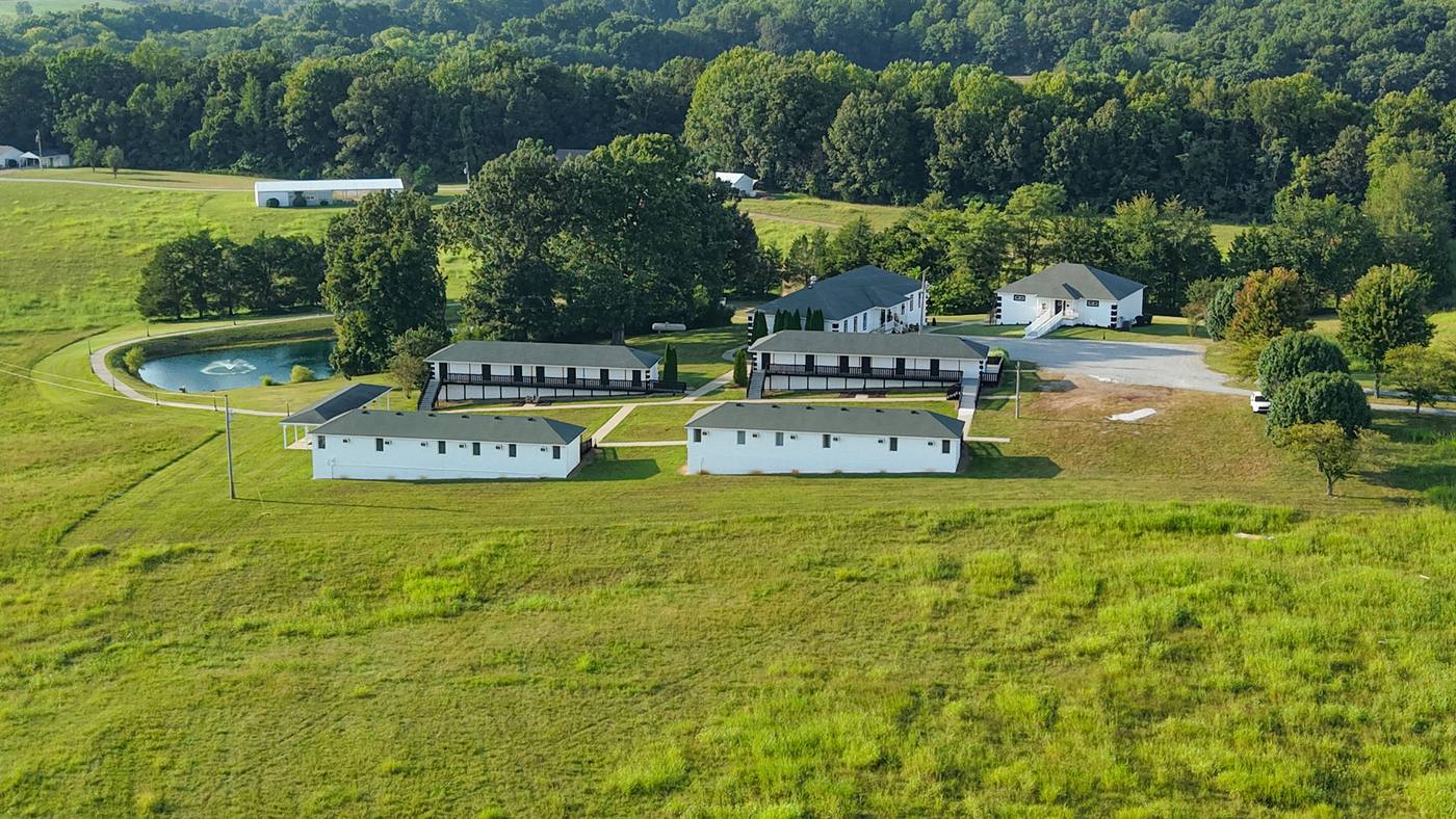 Aerial view of the whole ranch with the pond, residence buildings, pavilion and gravel drive across mown fields